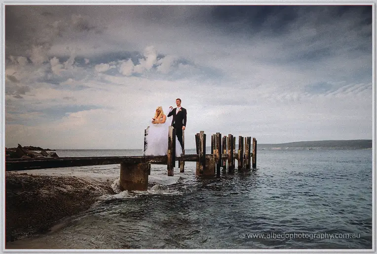Steph and Luke at the end of a weathered timber jetty, the groom lifting his bride's veil
