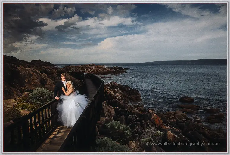 Steph resting against Luke on a cliffside boardwalk overlooking the ocean at dusk