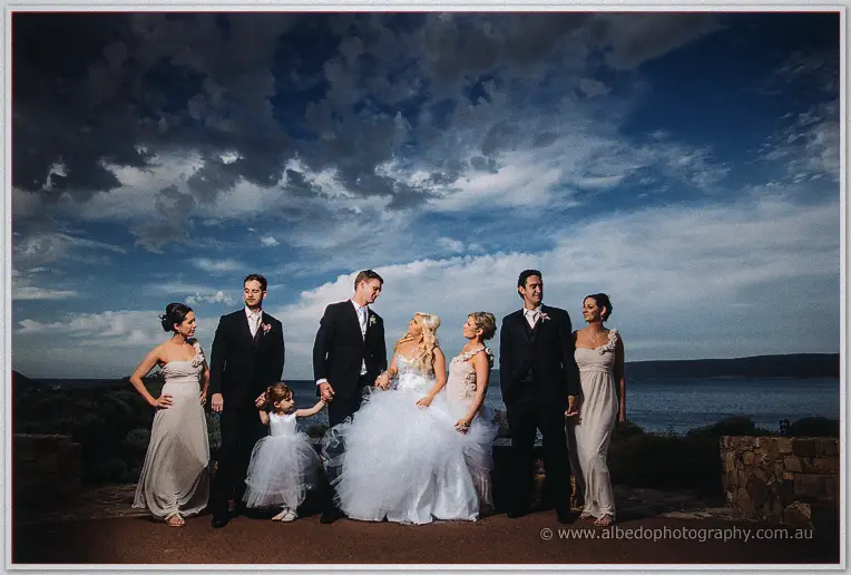 Full bridal party standing hand in hand before the ocean under a heavy evening sky