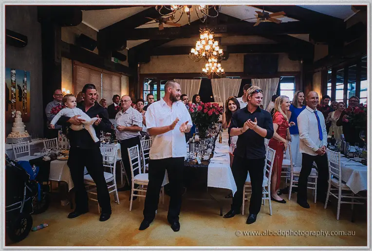 Guests on their feet applauding beneath the chandeliers of the timber reception room