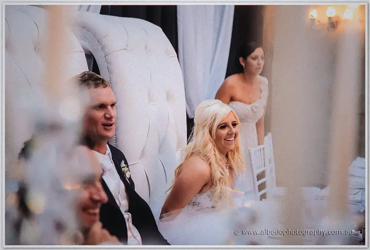Steph and Luke laughing on their tufted throne chairs during speeches at the reception