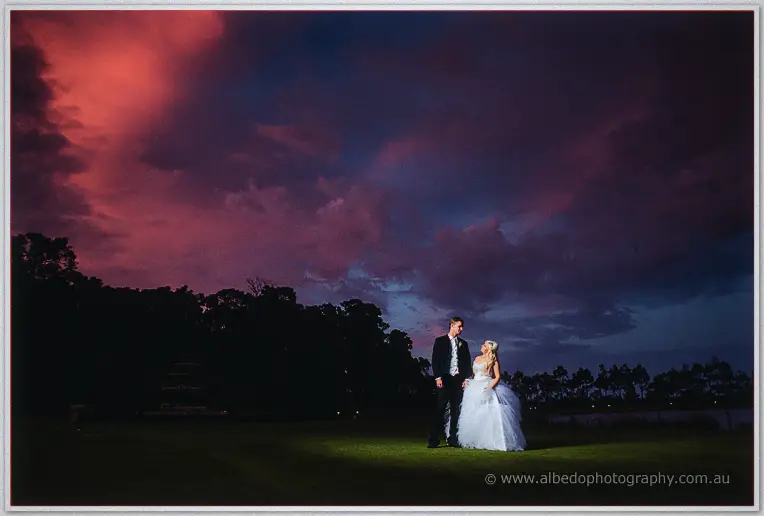 Couple facing each other across the lawn at nightfall under a crimson-streaked sky