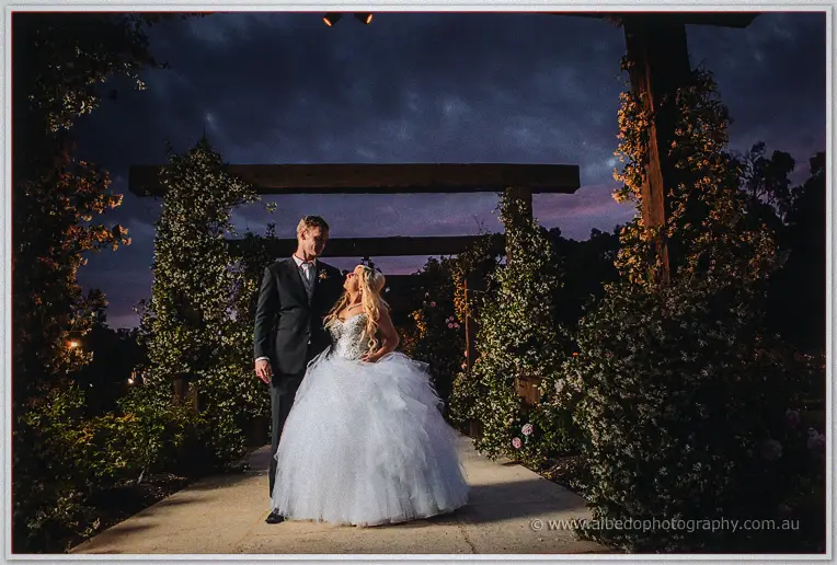 Couple gazing at each other under the timber rose arbor in the garden after dark