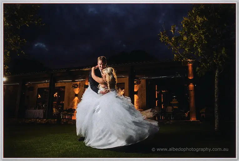 Luke spinning Steph in a dance on the dark lawn, the venue's warm lights behind them