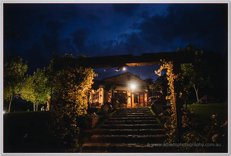 Stone steps and timber arbor leading up to the softly lit winery building at night