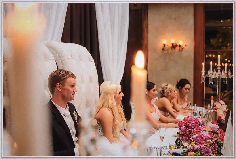 Bridal table listening to speeches past tall lit candles and deep pink roses