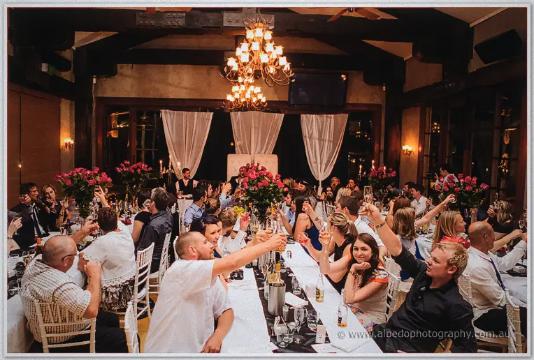 Guests raising glasses for a toast under the chandeliers of the packed reception room