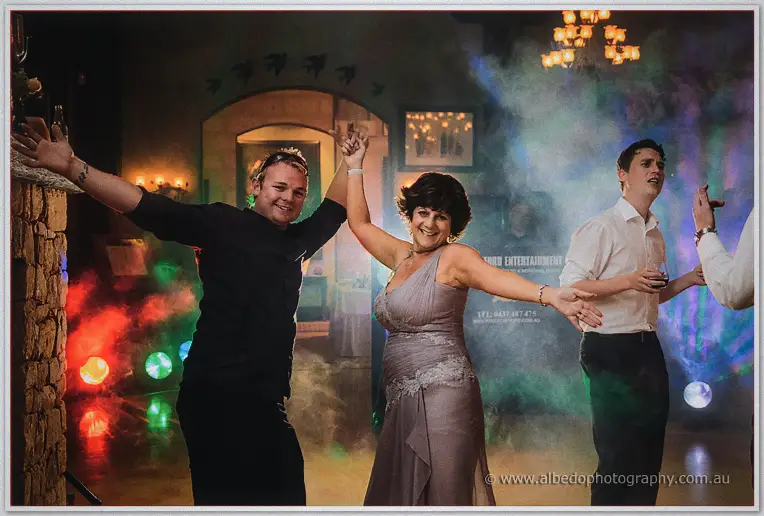 Guests dancing with arms wide amid green fog and coloured spotlights at the reception