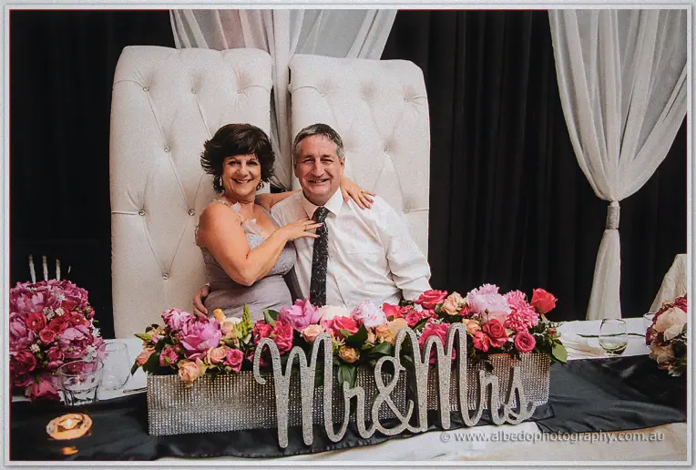 Parents of the couple seated on the white tufted throne chairs behind a Mr and Mrs sign