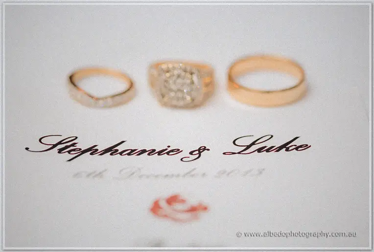 Gold bands and a diamond cluster ring resting above the Stephanie and Luke calligraphy