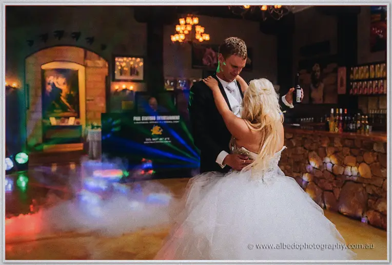 Bride and groom share their first dance through fog and coloured lights beside the winery's stone bar