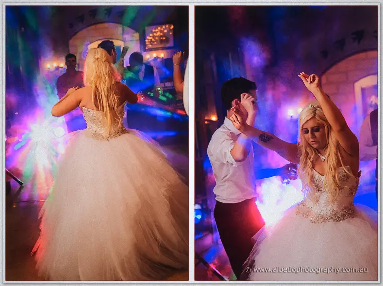 Bride dancing with arms raised among guests as pink and blue party lights fill the reception