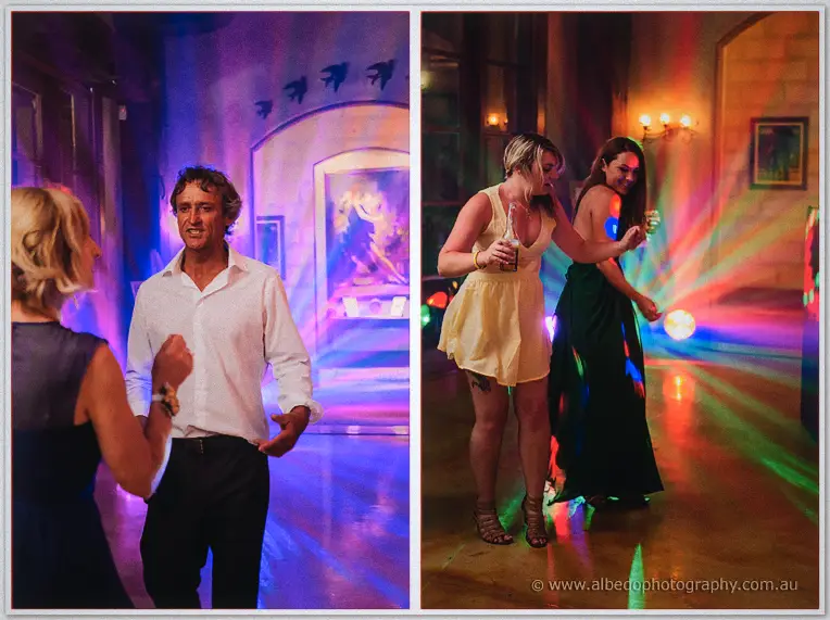 Wedding guests dance under rainbow light beams, two women twirling in summer dresses at the reception