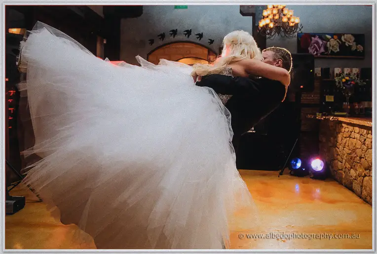 Groom swings his bride across the dance floor, her tulle skirt billowing under the chandelier