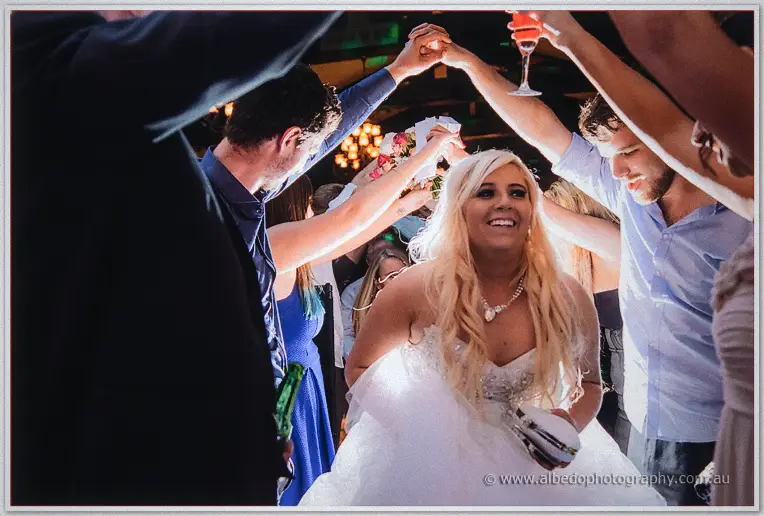 Bride beams as guests dance in a circle around her with raised arms at the winery reception
