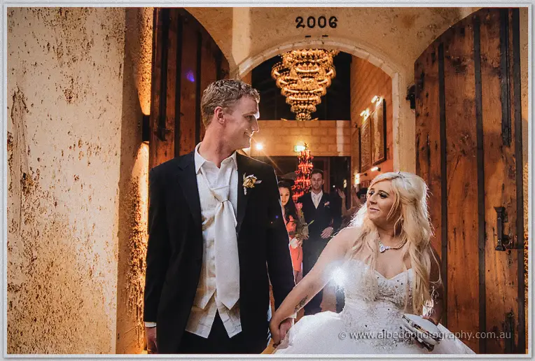 Newlyweds walk hand in hand through the winery's aged timber doors beneath a chandelier