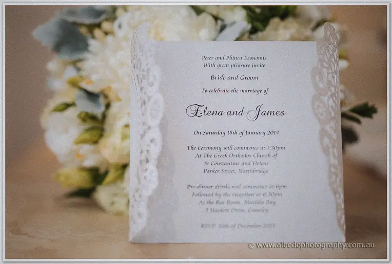 Lace-edged invitation to Elena and James's church wedding propped before white hydrangeas