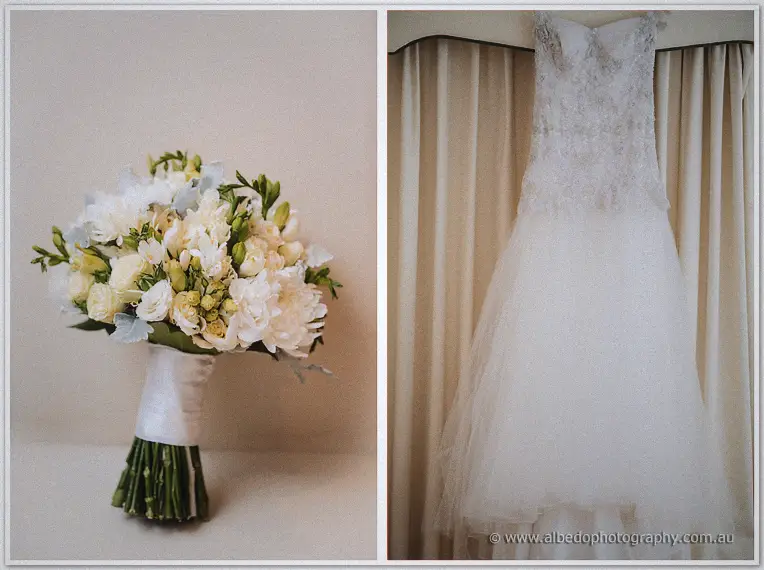Elena's white freesia bouquet beside her lace bodice and tulle gown hanging before cream curtains