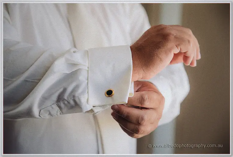 Close-up of hands fastening a gold-rimmed onyx cufflink on a white dress shirt