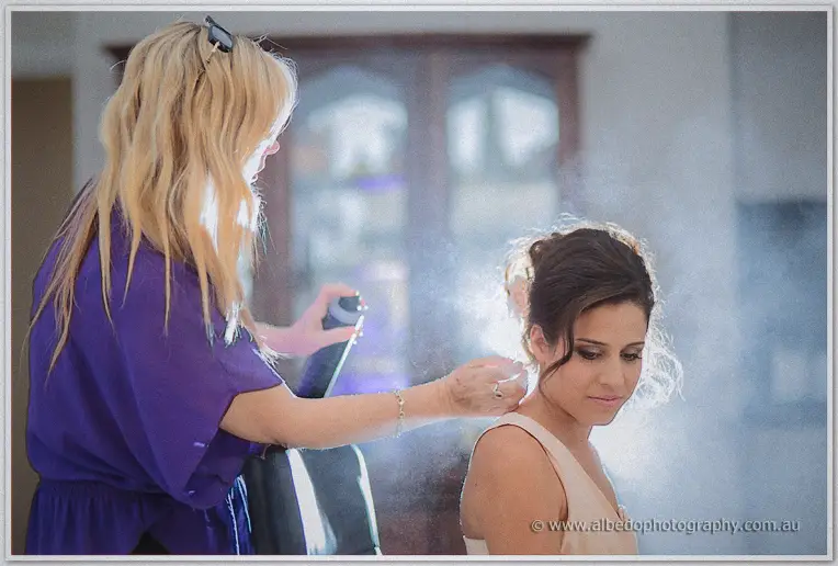 A stylist in purple hairsprays Elena's pinned curls before the Northbridge ceremony