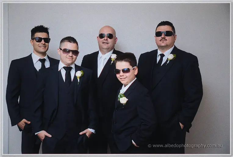 James and four groomsmen in black suits and aviators pose with their page boy