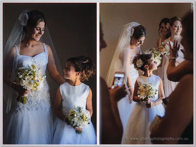 Elena and her flower girl smile with bouquets as a guest photographs the moment on a phone
