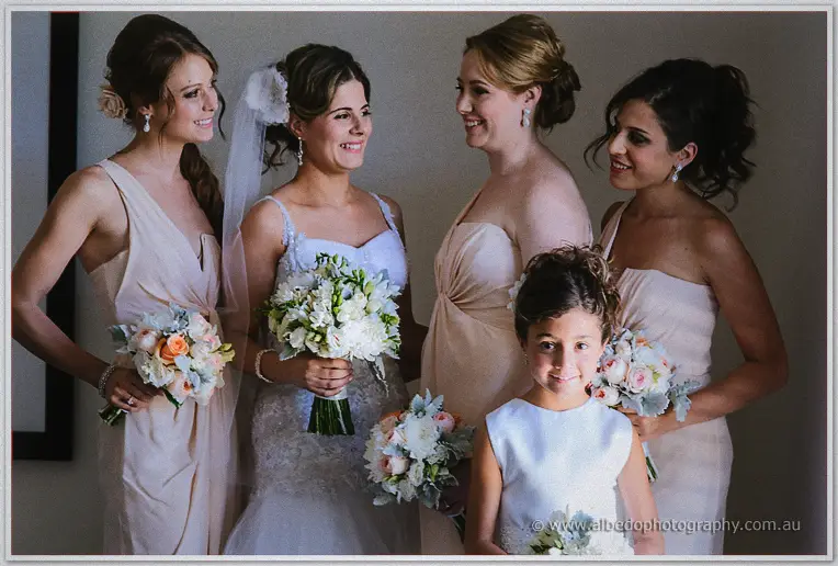 Elena laughs between three blush-gowned bridesmaids and her white-dressed flower girl