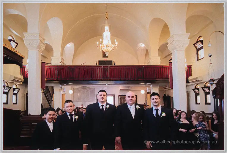James and his groomsmen wait beneath the chandelier as guests settle into the pews