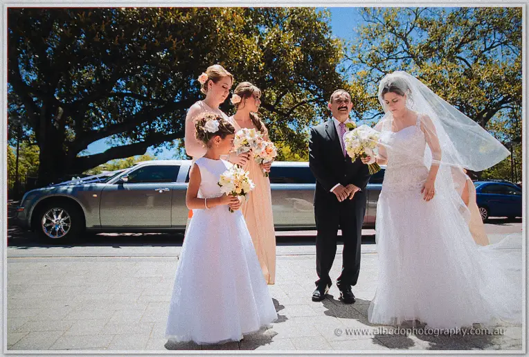 Elena, her father, flower girl and blush bridesmaids gather before the silver limousine