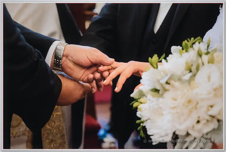Close-up of the gold ring sliding onto Elena's finger beside her white freesia bouquet