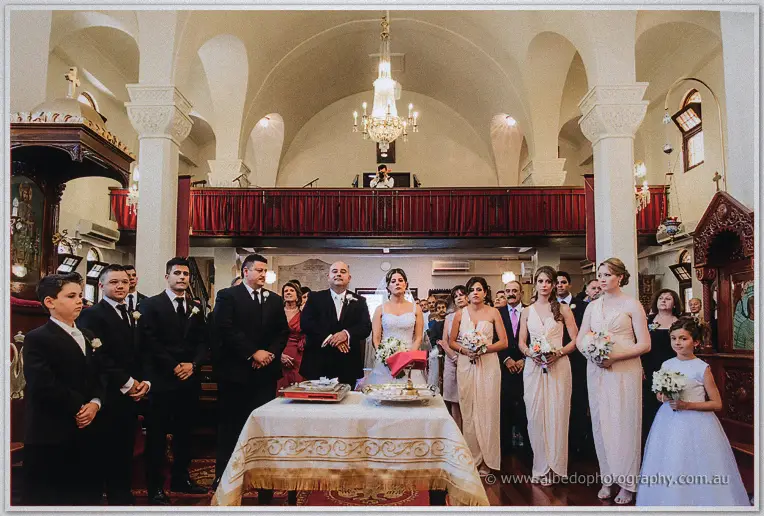 Bridal party and guests crowd around the ceremony table beneath the red-curtained loft