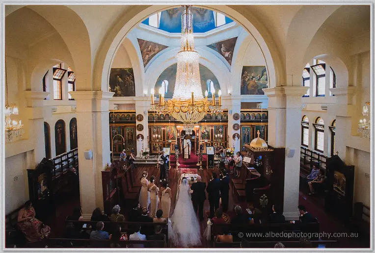 Elevated view of the couple before the gold iconostasis beneath the dome frescoes and chandelier