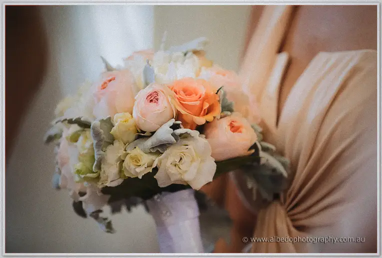 Bridesmaid's peach rose and dusty miller bouquet against her champagne gown