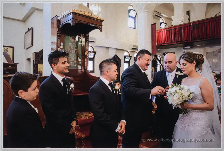 The mustached koumbaro exchanges rings as James, Elena and young attendants watch