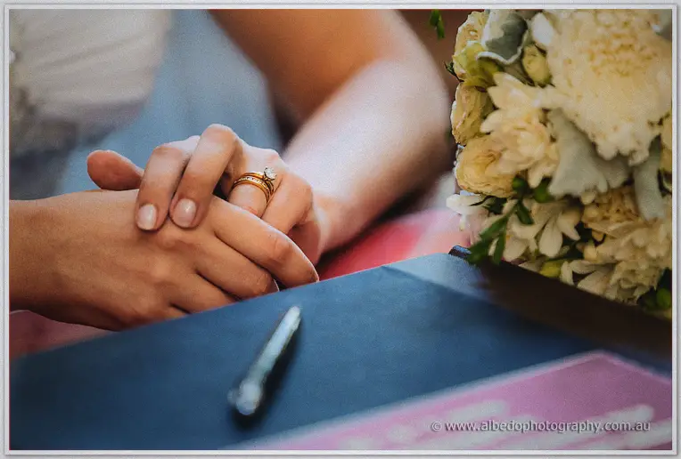 Elena's new gold ring glints on her folded hands beside a silver pen and cream bouquet