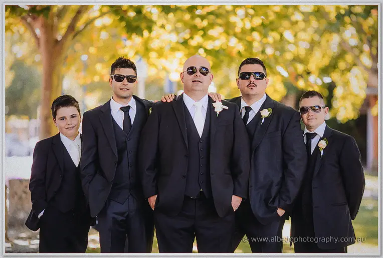 James stands with his groomsmen and a page boy, all in black suits and sunglasses under golden leaves