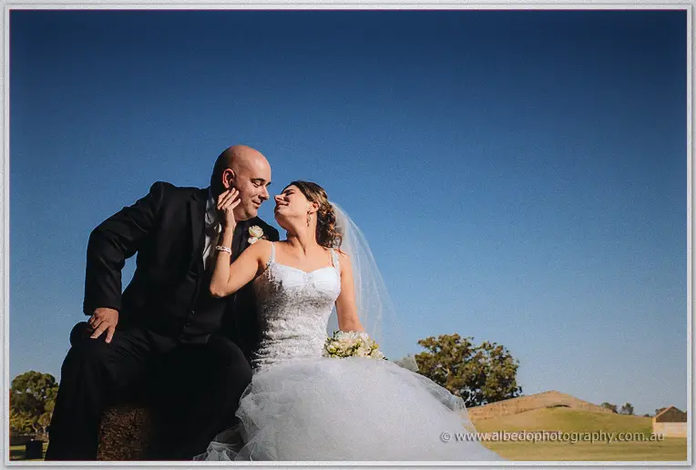 Elena strokes James's cheek as the pair grin at each other, low sun raking across parkland grass behind them