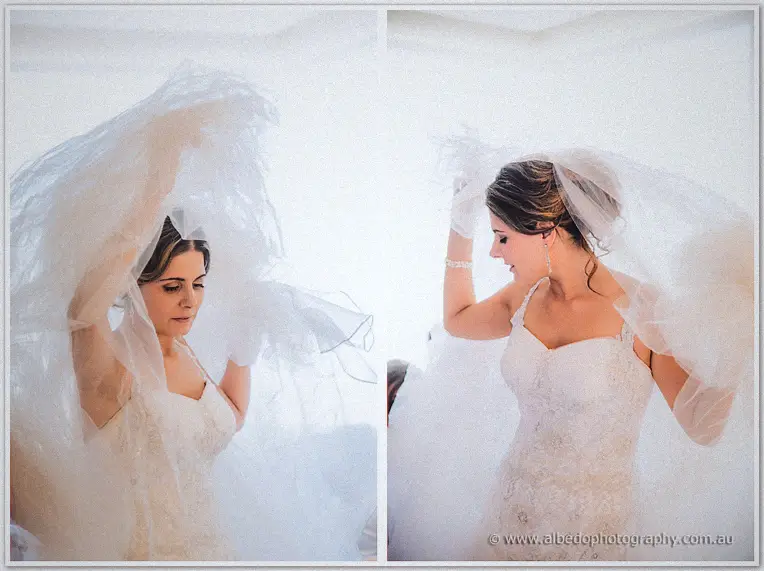 Elena lifts her frothy veil over her updo in soft window light during bridal preparations