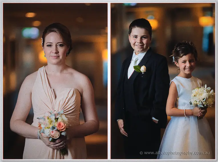 A peach-gowned bridesmaid and two smiling children in white hold pastel bouquets in the glowing hotel corridor