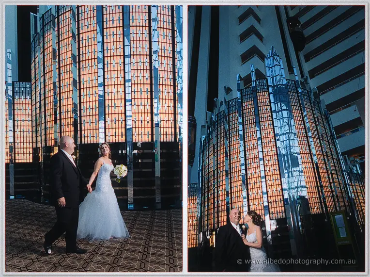 James leads Elena past towering mirrored panels glowing amber inside the hotel's grand atrium
