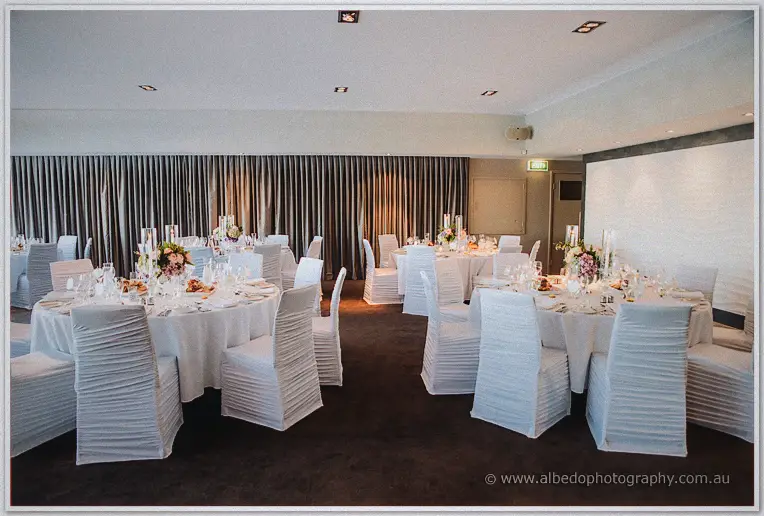 Round tables with white chair covers and pink florals await guests in the Matilda Bay reception room