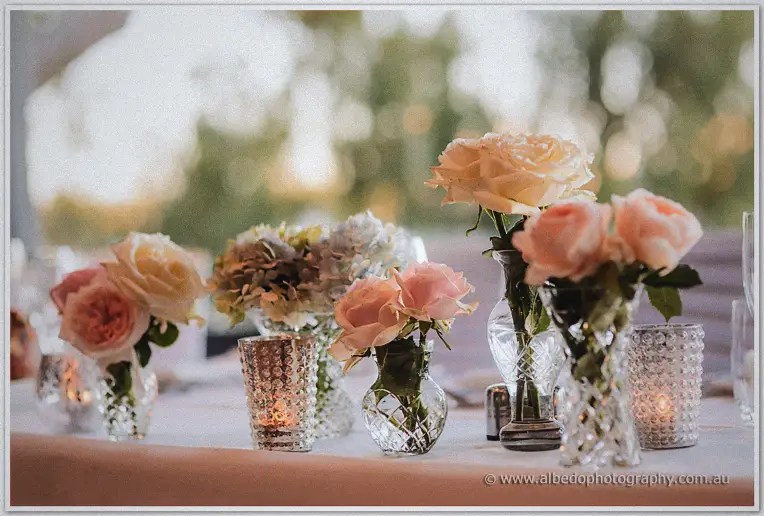 Cut-crystal vases of peach roses and hydrangeas catch the last warm light on the bridal table