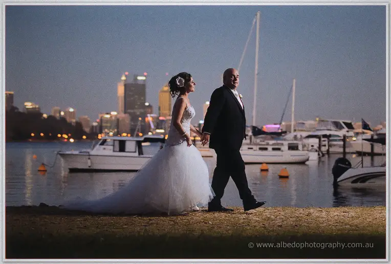 James leads Elena by the hand along the foreshore past moored boats, city lights shimmering on the Swan River
