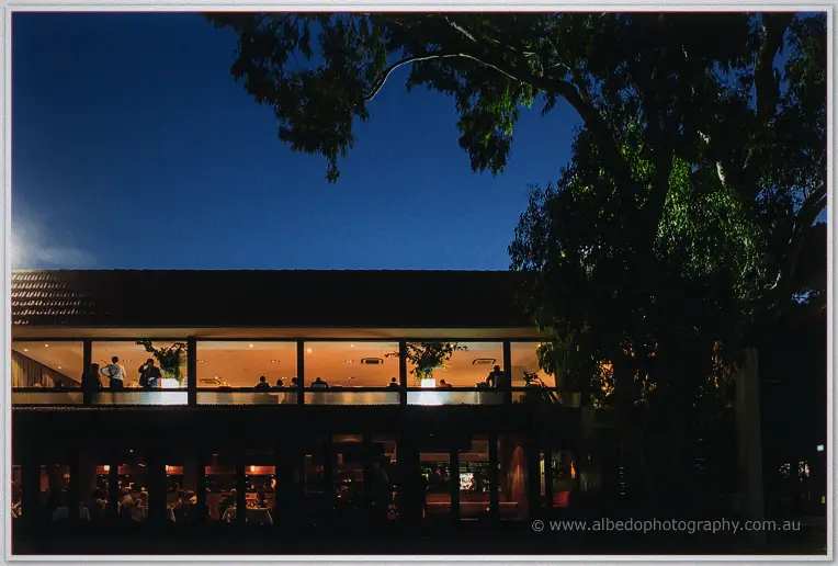 Guests mingle in the warmly lit glass frontage of the Matilda Bay venue beneath a deep blue evening sky