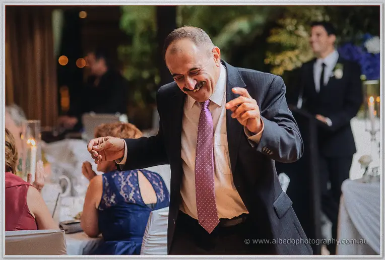 An older guest in a purple tie dances joyfully between the tables as the reception gets underway