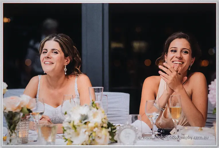 Two bridesmaids laughing at the speeches, candlelit Matilda Bay bridal table with blush flowers before them