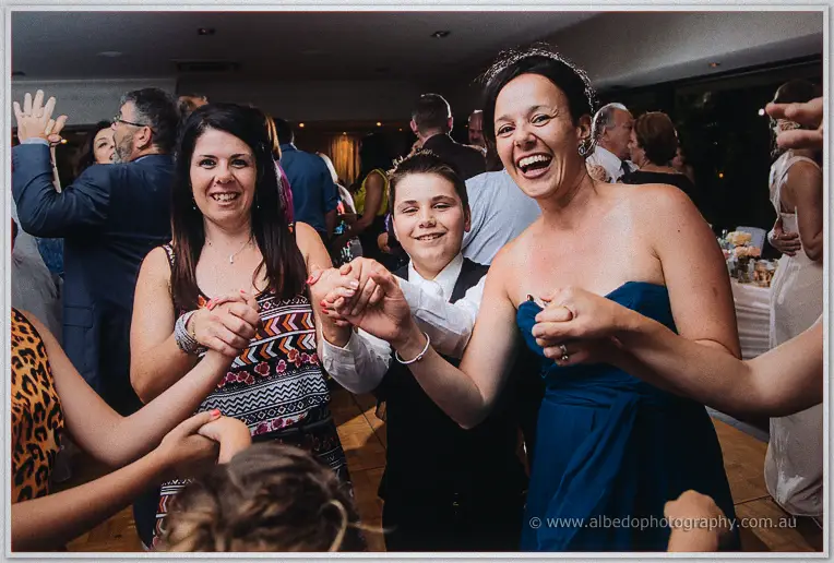 Guests in party dresses dancing with linked hands, a woman in teal laughing on the Matilda Bay dance floor