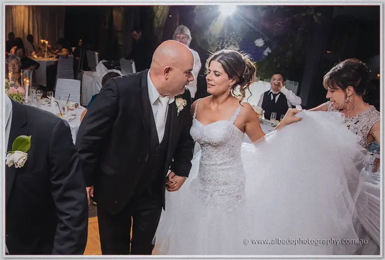 Groom in a white tie leading his bride, her tulle skirt lifted, back through the candlelit reception tables