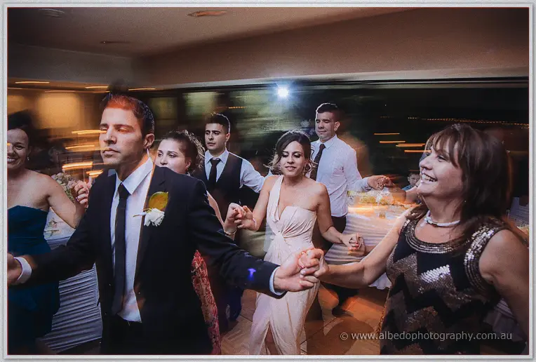 Groomsman and bridesmaid dancing in a long snaking line of guests, streaked lights around them