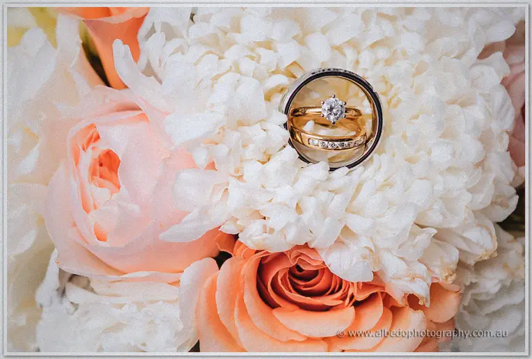 Two gold wedding rings nestled in white chrysanthemums and peach garden roses of the bridal bouquet